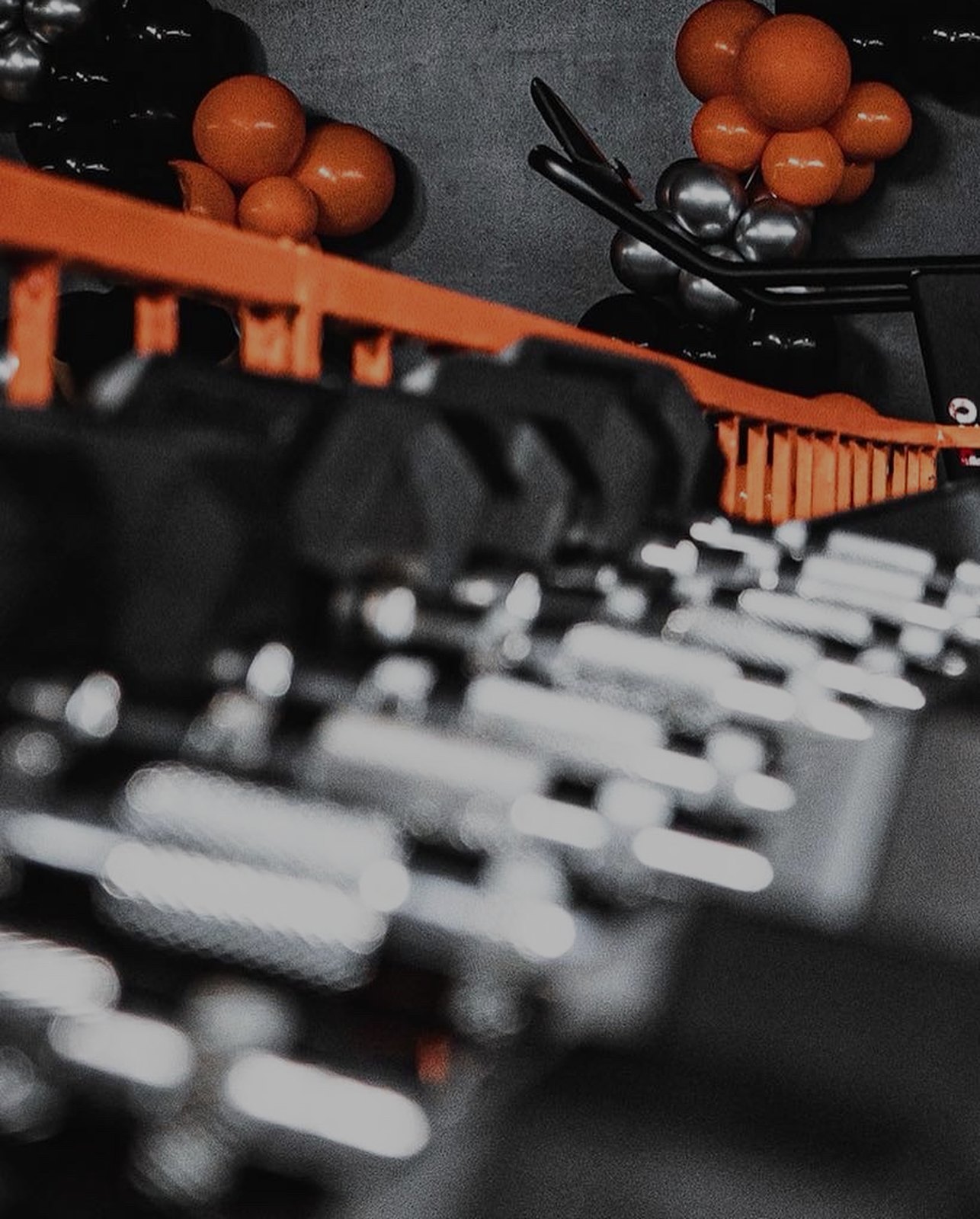 Dumbbell rack with orange rails and black and orange balloons inside the MorrFit studio